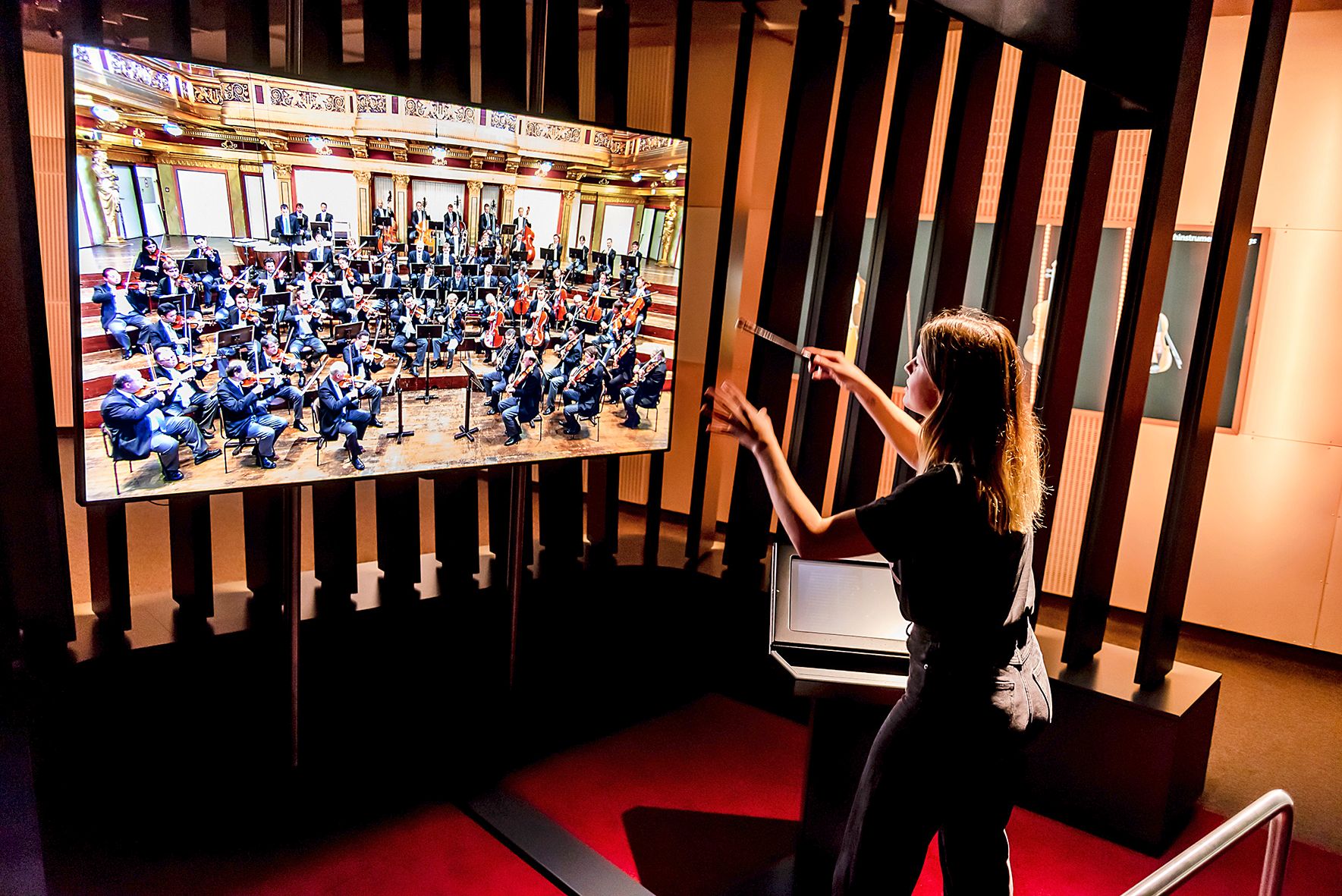 Person dirigiert virtuelles Orchester auf Bildschirm im Haus der Musik.