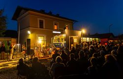 In der warmen Abenddämmerung versammeln sich Menschen vor dem Kulturbahnhof, um die Klänge eines Live-Konzerts zu genießen. Die Atmosphäre ist erfüllt von Musik und Lichtern, während die historische Kulisse des Bahnhofs eine besondere Stimmung schafft. Ein unvergesslicher Abend, der die Herzen der Besucher berührt.