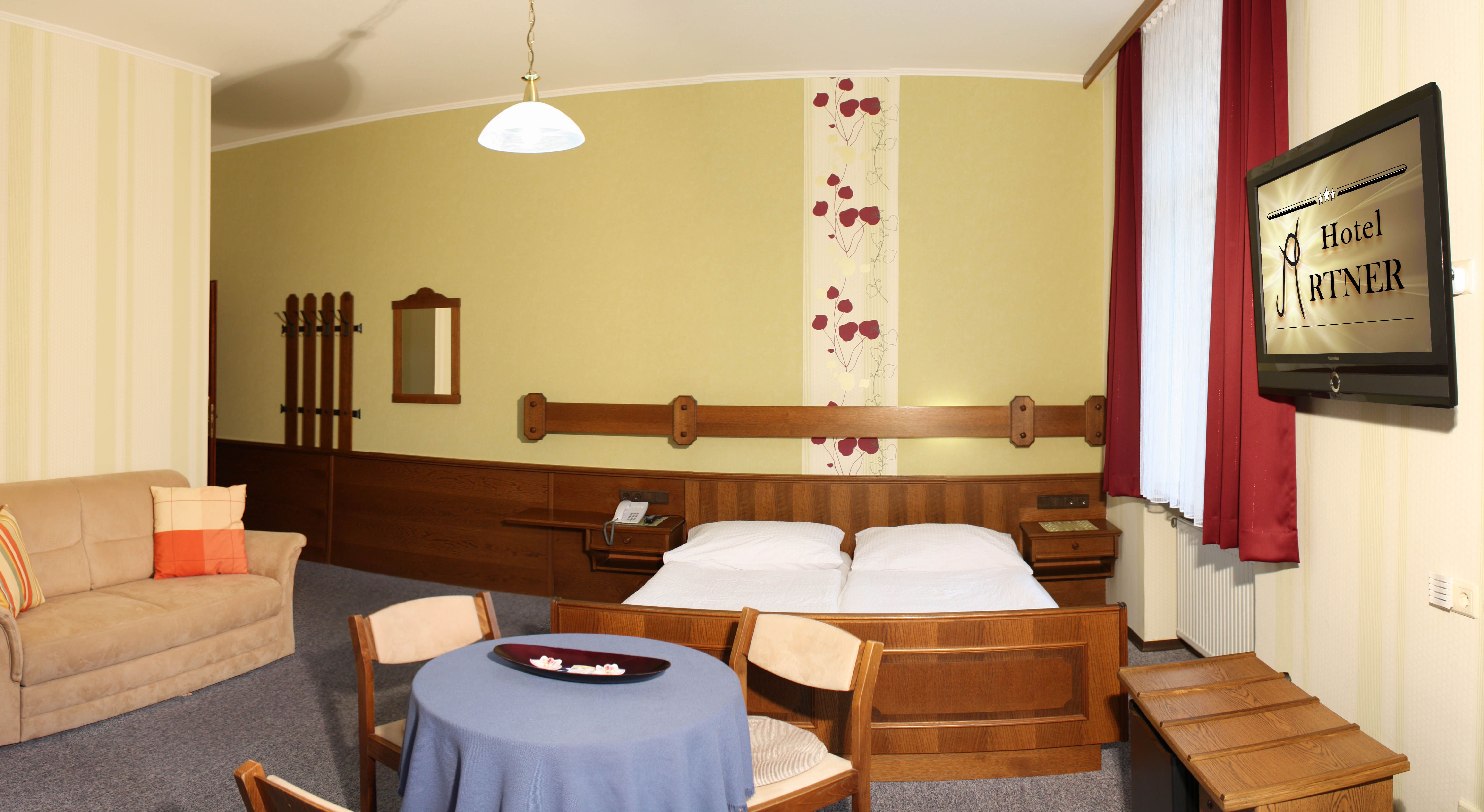 Hotelzimmer mit Doppelbett, Sofa, Tisch und Fernseher.