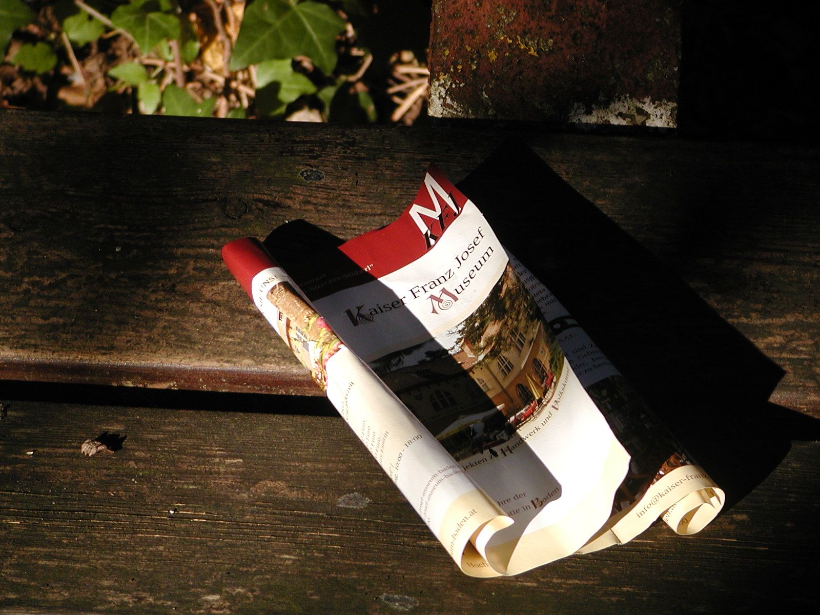 Zusammengerolltes Prospekt des Kaiser-Franz-Josef-Museums auf einer Holzbank.