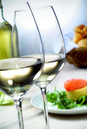 Zwei gefüllte Weingläser mit Weißwein, im Hintergrund ein Teller mit Lachs und Salat.