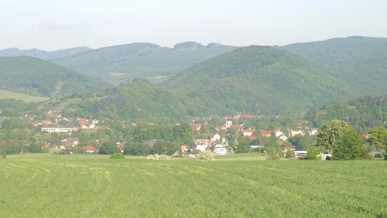 Landschaftsansicht von Alland mit grünen Feldern und bewaldeten Hügeln im Hintergrund.