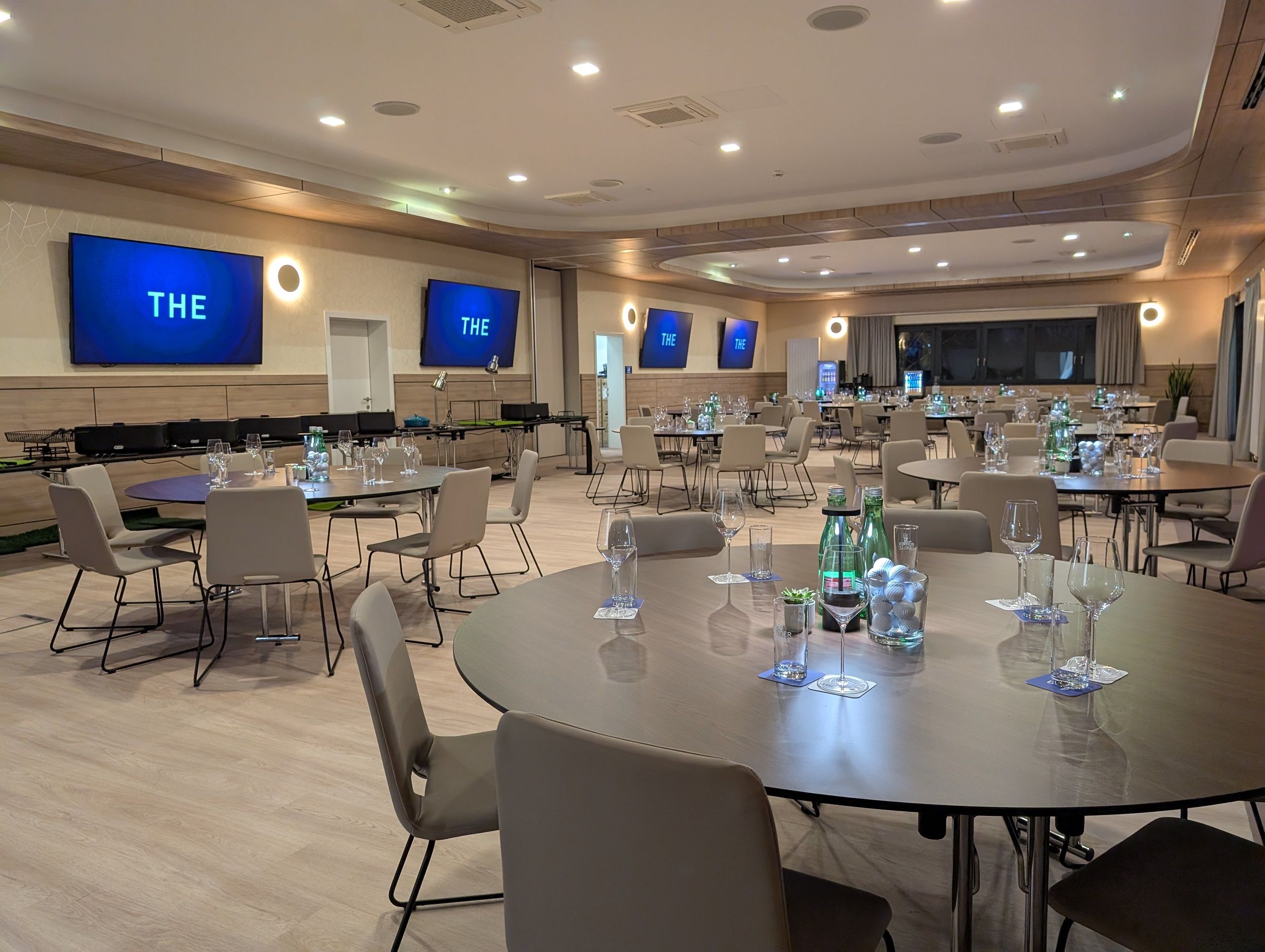 Moderner Seminarraum mit runden Tischen, Stühlen und Bildschirmen an den Wänden.