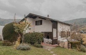 Ein zweistöckiges Haus mit Garten und Terrasse, umgeben von Bäumen und Sträuchern.