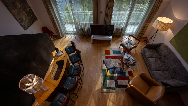 Wohnzimmer mit moderner Einrichtung, buntem Teppich und großen Fenstern.