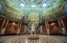 Prunksaal der Österreichischen Nationalbibliothek mit Statue und Deckenfresken.