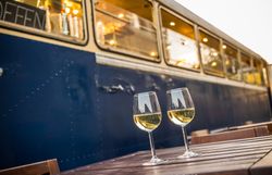 Genießen Sie einen entspannten Abend auf der Terrasse des Kulturbahnhofs, wo zwei Gläser erfrischender Weißwein auf einem rustikalen Holztisch stehen. Die sanften Farben des Sonnenuntergangs spiegeln sich in den Gläsern wider und schaffen eine einladende Atmosphäre, die zum Verweilen einlädt.