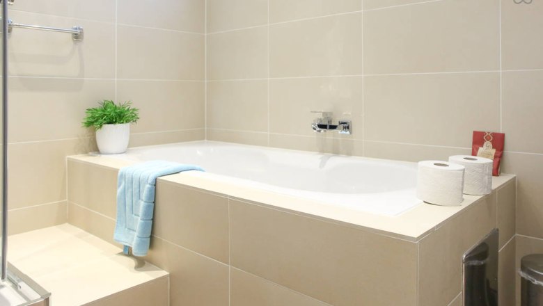 Modernes Badezimmer mit Badewanne, Handtuch, Pflanze und Toilettenpapier.