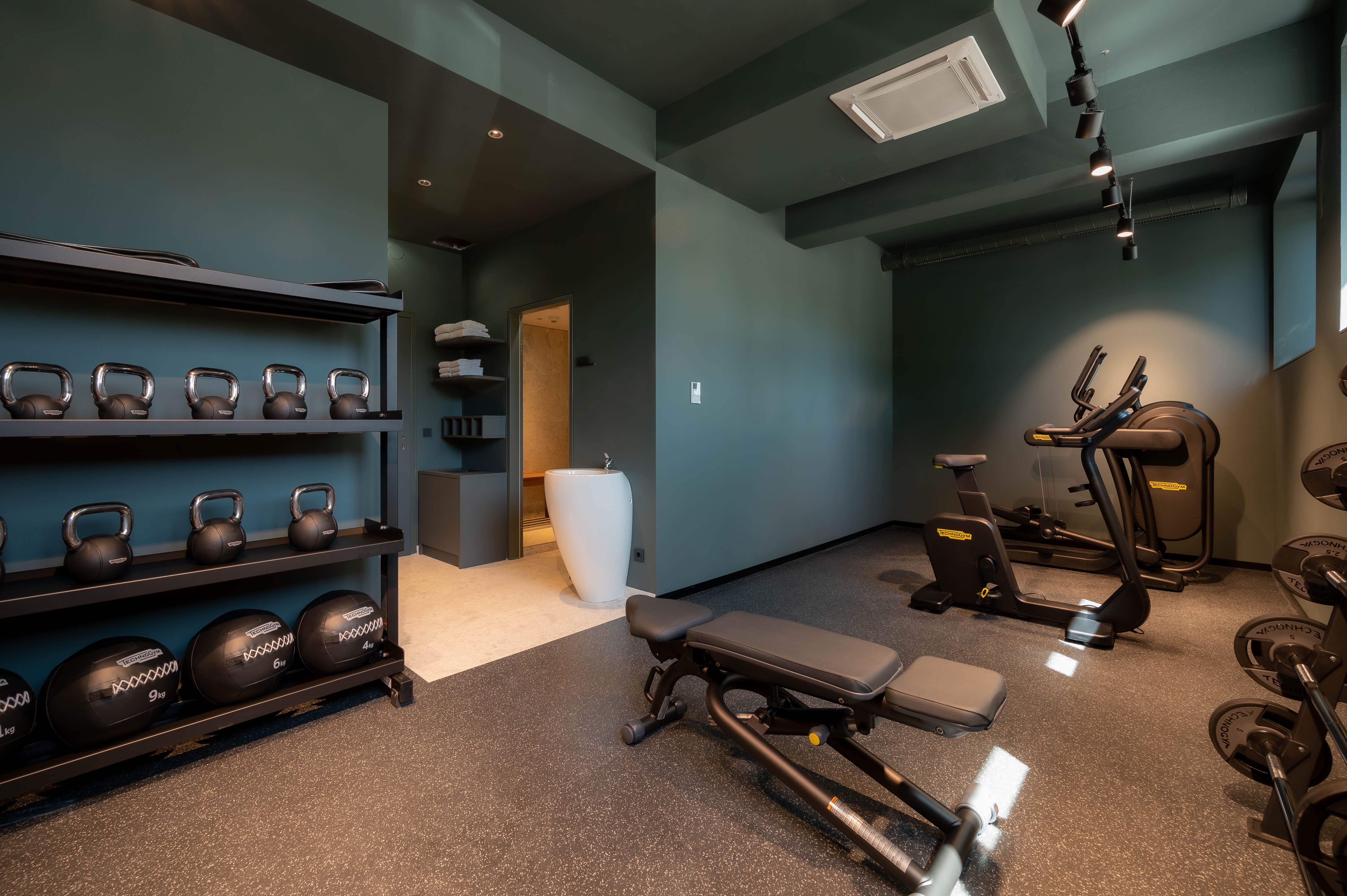 Moderner Fitnessraum mit Kettlebells, Hanteln, Laufband und Ergometer.