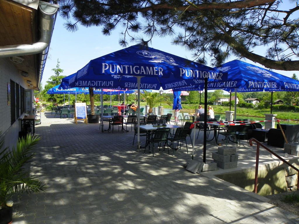 Außenbereich eines Gasthauses mit blauen Sonnenschirmen und Tischen.