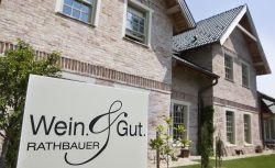 Ein Schild mit der Aufschrift 'Wein & Gut Rathbauer' vor einem Backsteingebäude.
