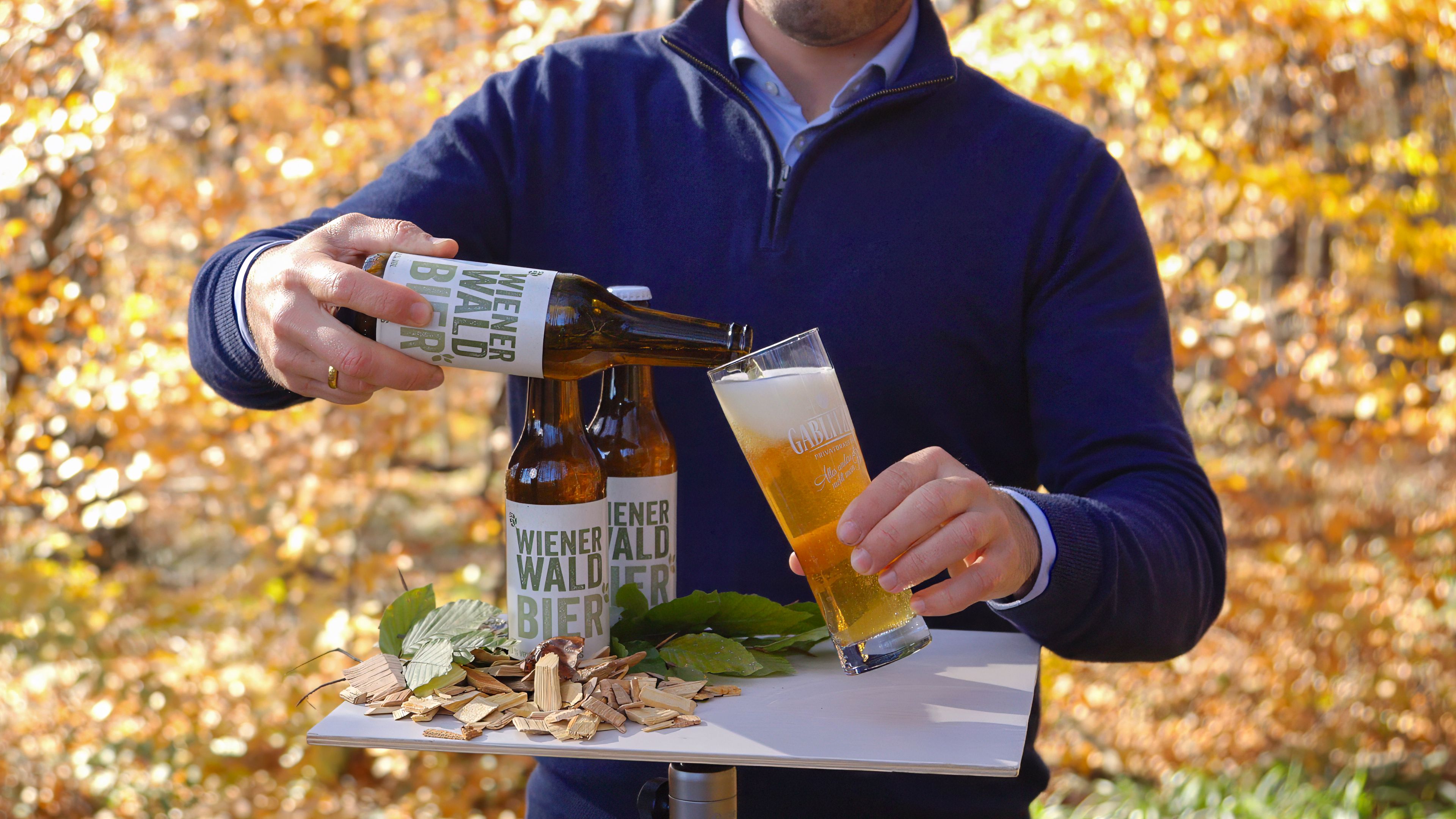 Arrangiert auf einem Tisch im herbstlich verfärbten Wienerwald wird das Wienerwaldbier in ein Glas gefüllt.