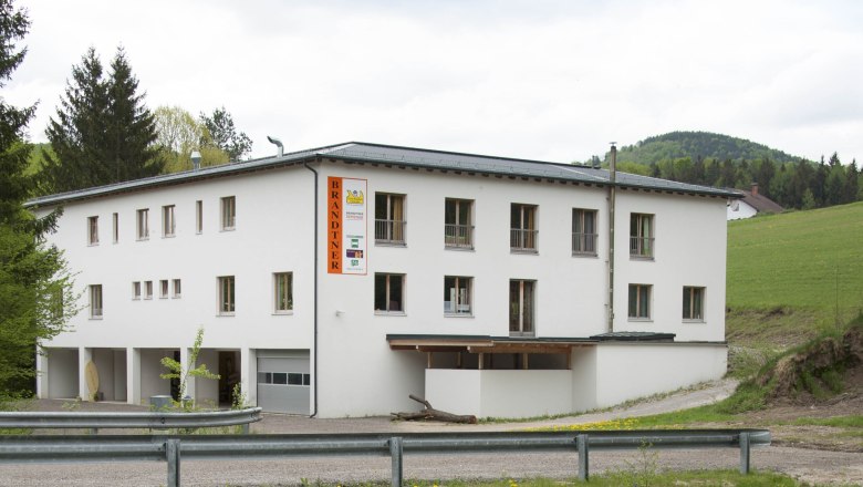 Ein weißes Gebäude mit der Aufschrift 'Brandtner' in ländlicher Umgebung.