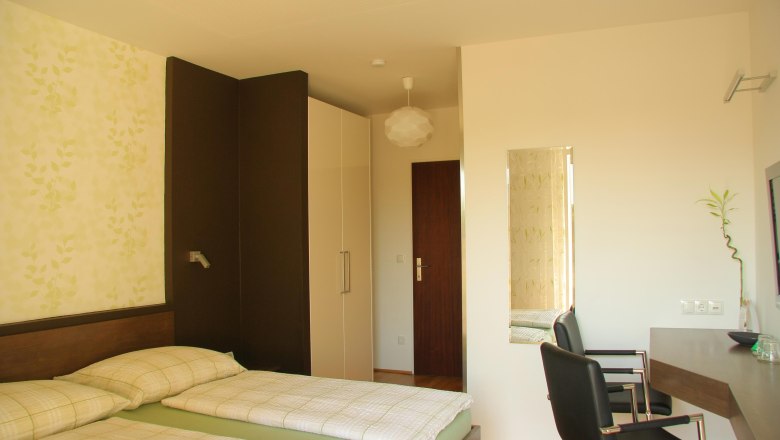 Ein modernes Hotelzimmer mit zwei Einzelbetten, einem Schreibtisch und einem Stuhl. Die Wände sind hell und mit einem Pflanzenmuster dekoriert.