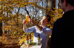 Im herbstlichen Wienerwald bei strahlendem Sonnenschein und gelblich orange verfärbten Blättern wird das Wienerwaldbier, eingeschenkt in einem Bierglas, von dem Guide in das Sonnenlicht gehalten.