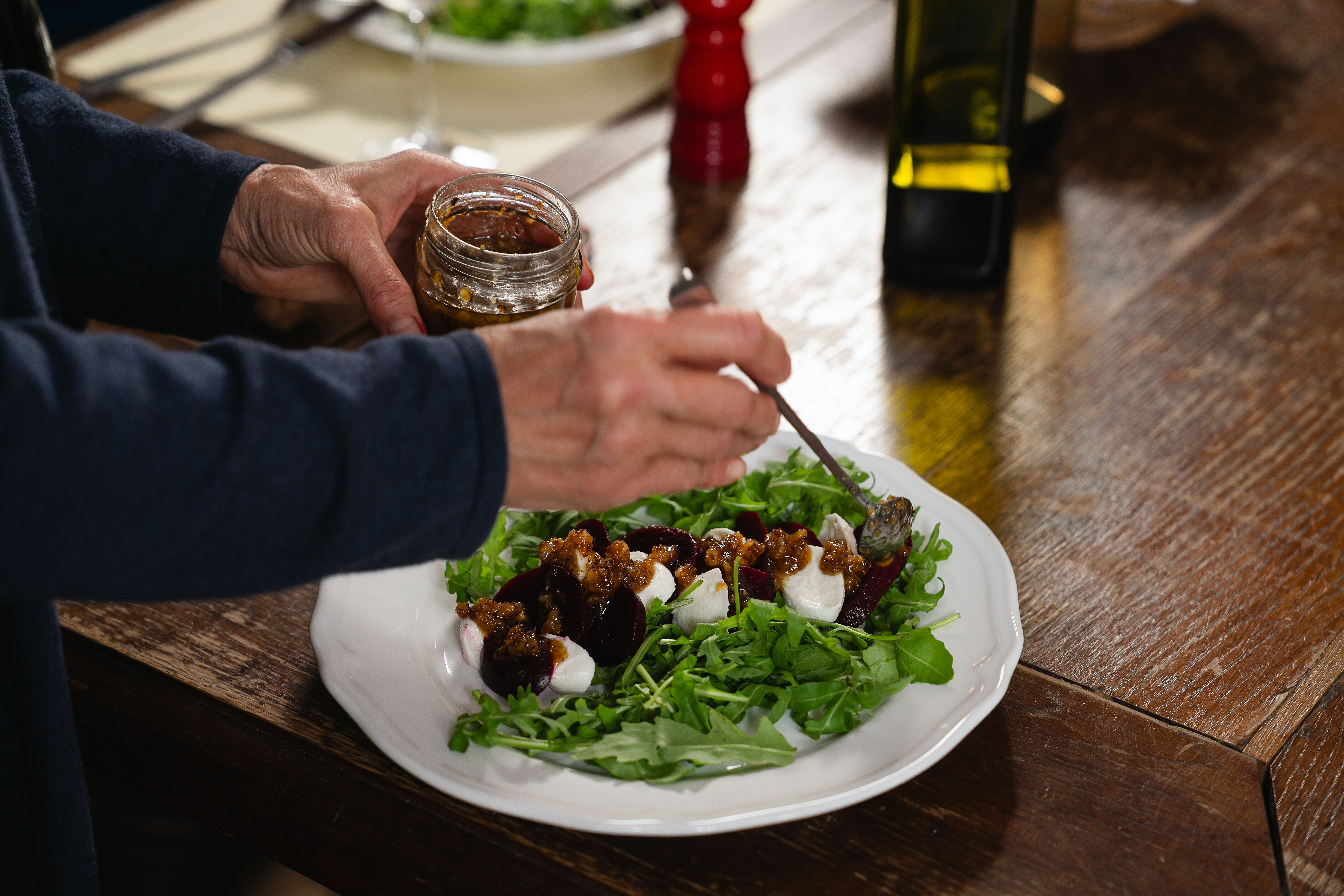 Ein Mozzarella-Rucola-Salat, verfeinert mit hauseigenen Chutneys, kunstvoll dekoriert auf einem rustikalen Holztisch beim Hauerhof 99. Dieses Arrangement verstärkt das authentische und einladende Ambiente des Heurigen.
