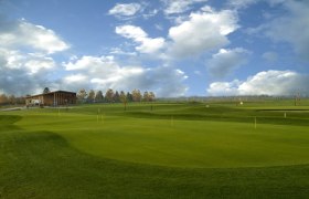 Golf course with clubhouse and cloudy sky.