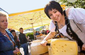 Woman in traditional dress cutting cheese at a market.