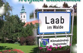 Willkommensschild von Laab im Walde mit Kirche im Hintergrund.