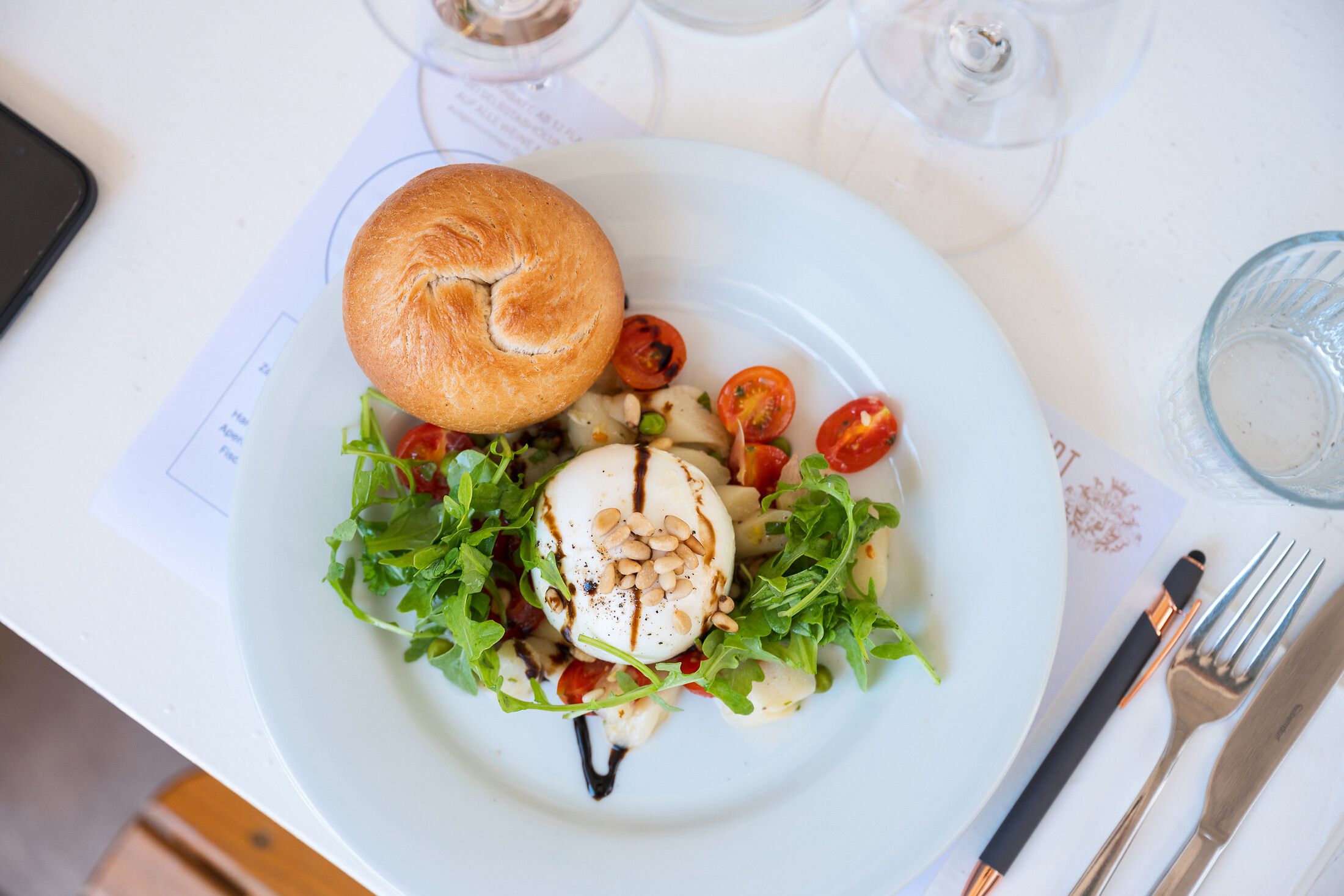 Mozzarella auf frischem Rucola mit halbierten Cocktailtomaten als Gang der Oldtimer Genusstour beim Heurigen, angerichtet auf einem weißen Tisch.