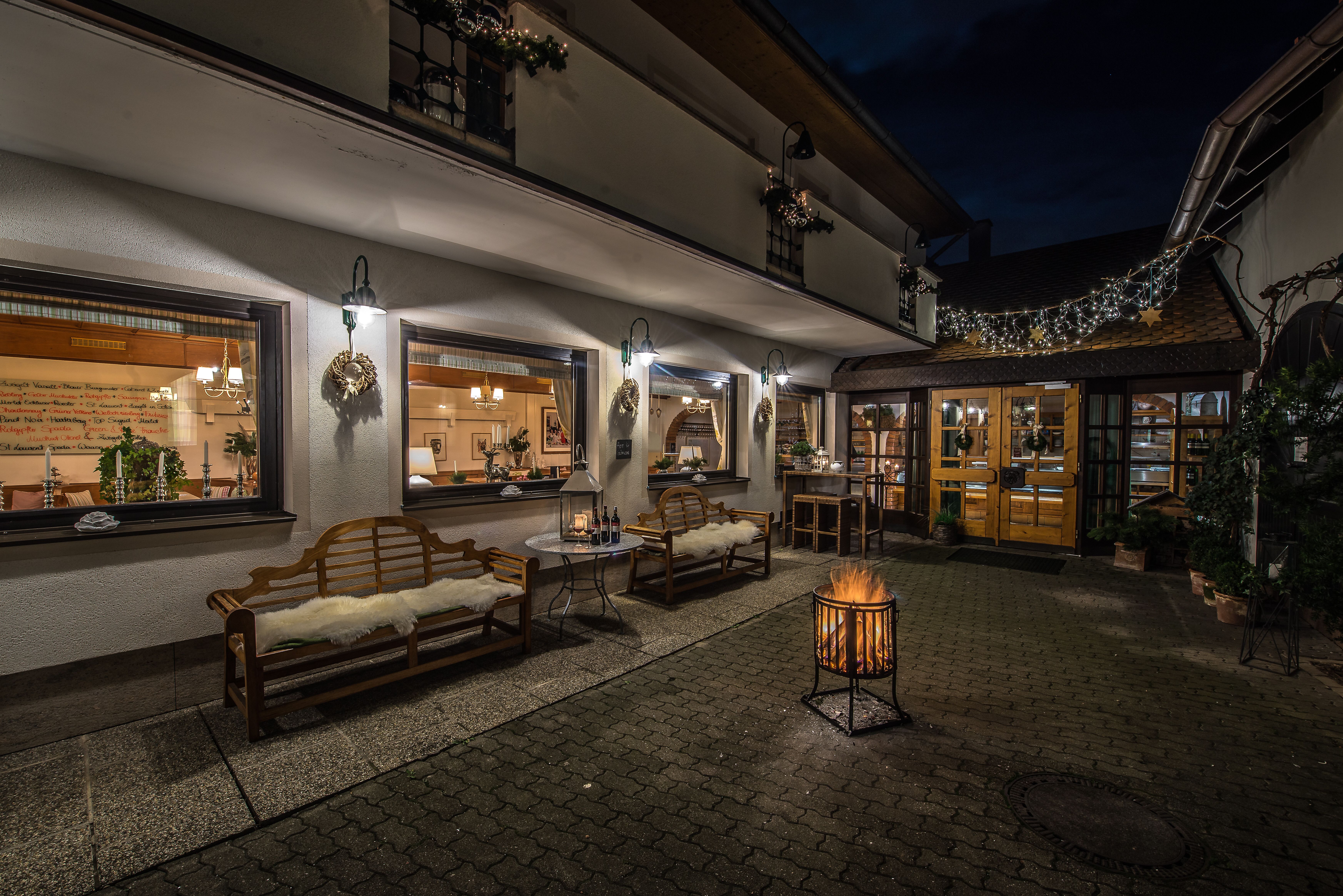 In der kühlen Abenddämmerung erstrahlt der Innenhof des Weinguts in warmem Licht. Gemütliche Sitzgelegenheiten laden dazu ein, die frische Luft und die ruhige Atmosphäre zu genießen, während der Duft von Wein und regionalen Köstlichkeiten in der Luft liegt.