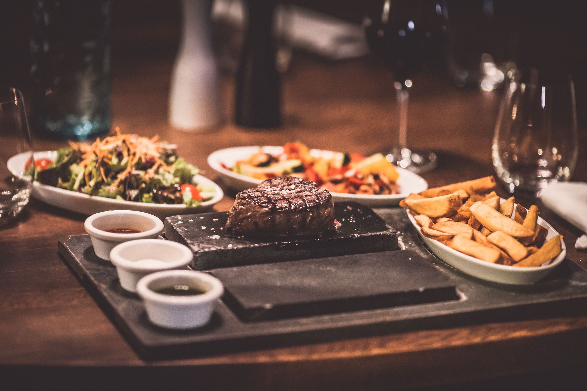 Ein Teller mit Steak und Pommes, daneben Salat und Soßen auf einem Tisch.