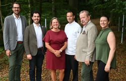 Gruppe von Personen steht vor einem Wald für ein Gruppenfoto