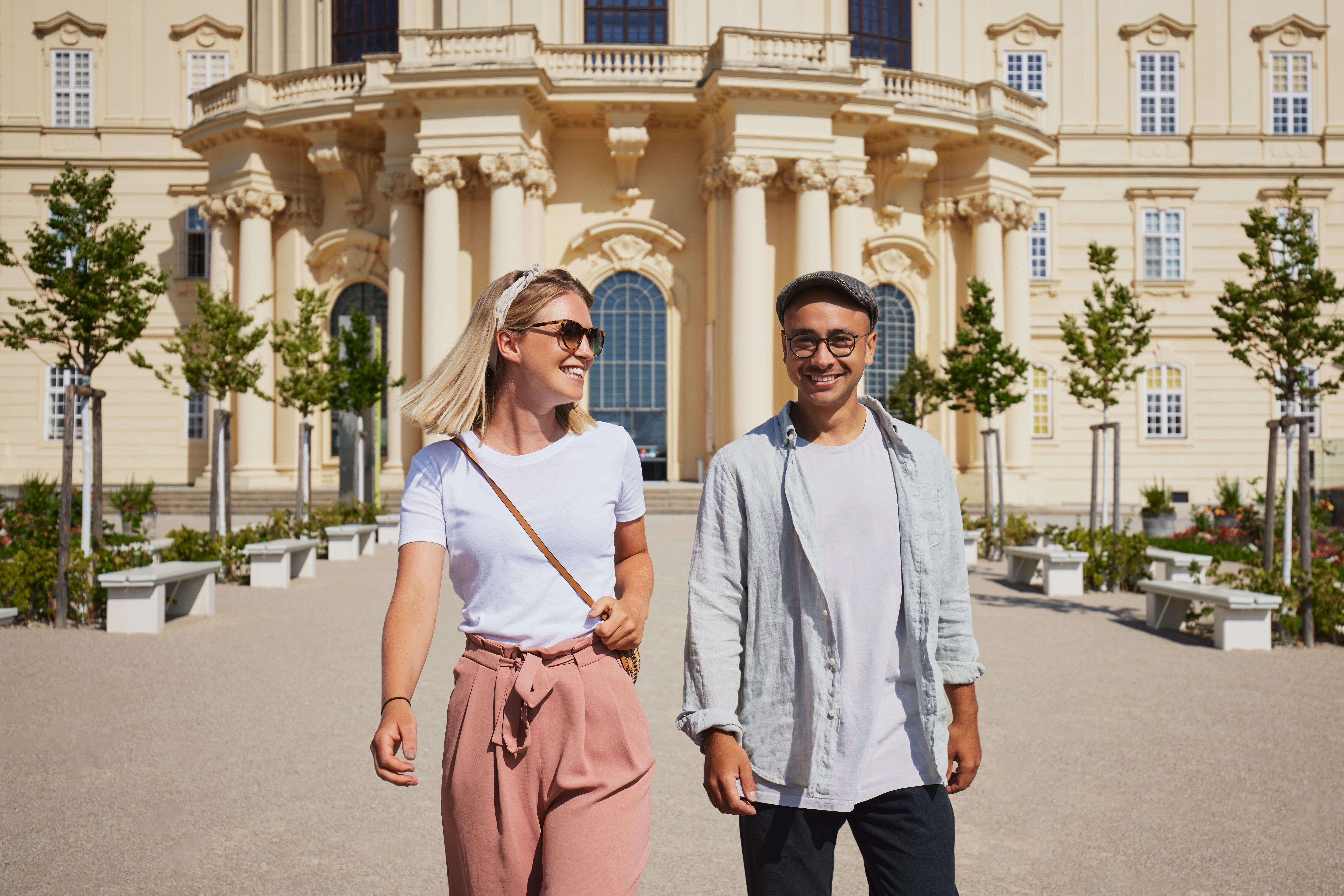 Ein sonniger Tag lädt zu einem entspannten Spaziergang ein, während die frische Luft und die blühenden Pflanzen die Sinne beleben. Zwei Freunde genießen die harmonische Atmosphäre und die beeindruckende Architektur im Hintergrund, die den perfekten Rahmen für unvergessliche Erinnerungen bietet.