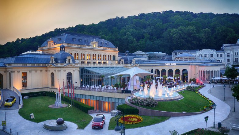 Außenansicht des Congress Centers Baden mit beleuchtetem Springbrunnen und umliegender Natur.