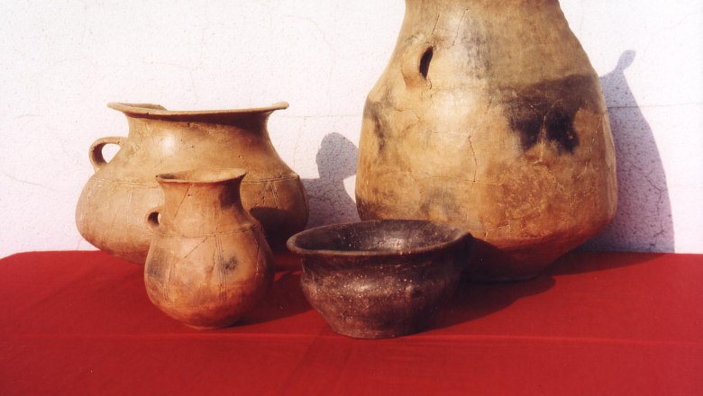 Four antique clay vessels on red cloth in front of a white wall.