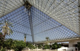 Innenansicht einer großen Glaspyramide mit Pflanzen und Palmen.