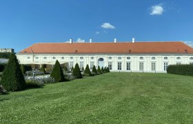 Geb&auml;ude mit rotem Dach und wei&szlig;en W&auml;nden im Augarten, umgeben von gepflegtem Rasen und B&auml;umen.