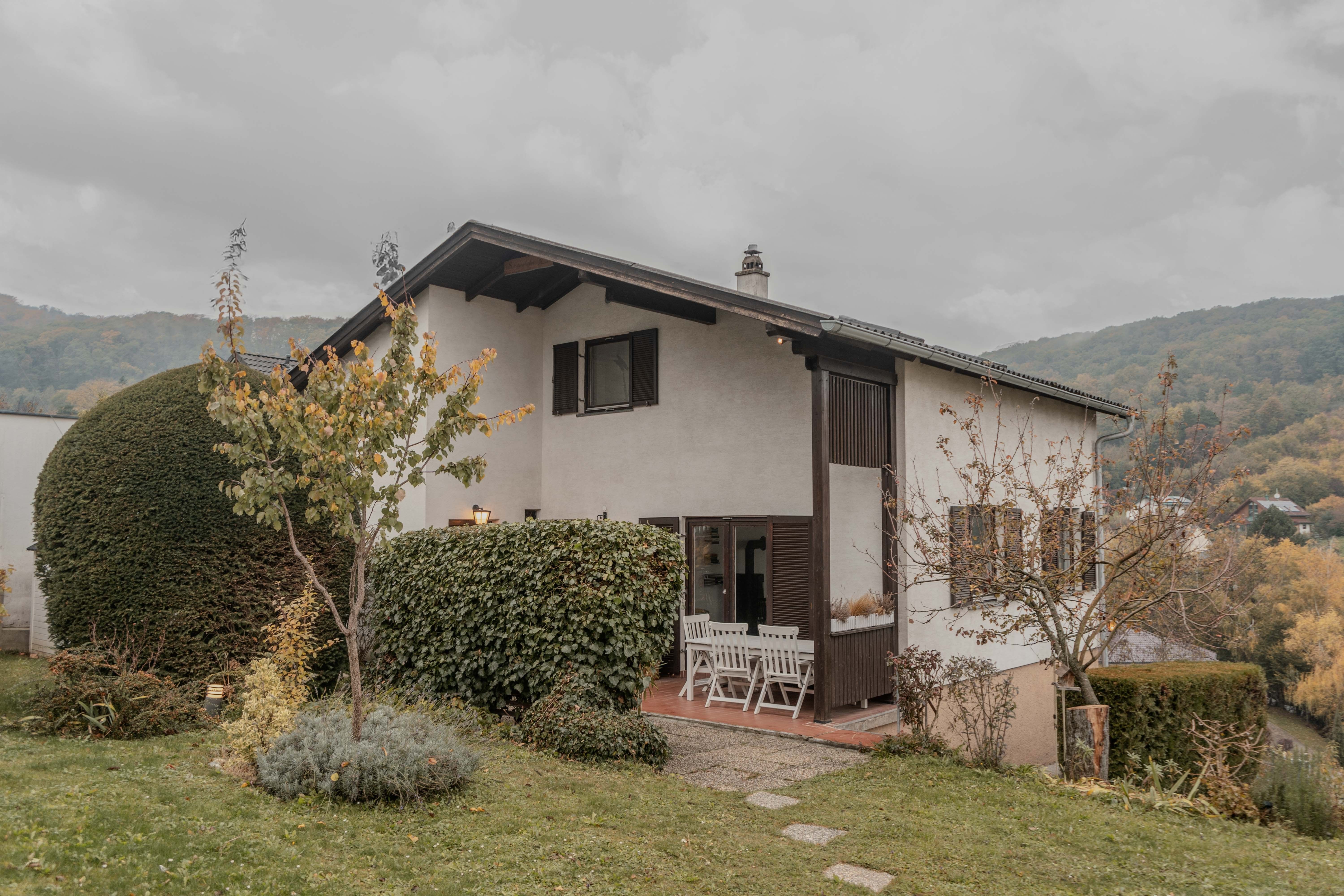 Ein zweistöckiges Haus mit Garten und Terrasse, umgeben von Bäumen und Sträuchern.