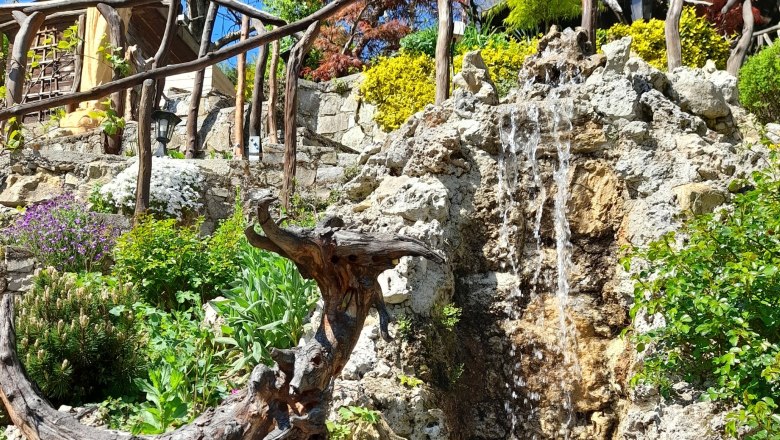Garten mit Statue, Wasserfall und bunten Pflanzen.