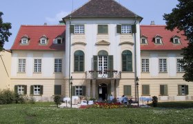 Frontansicht von Schloss Hunyadi mit Garten und Blumenbeeten.