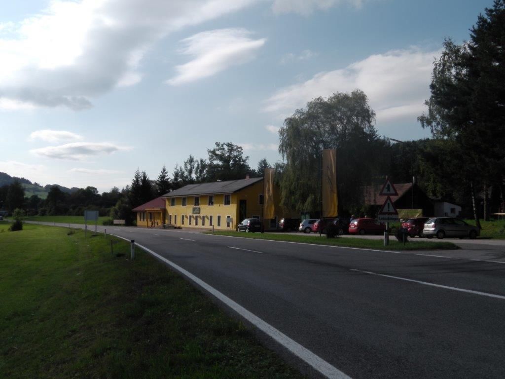 Ein gelbes Gebäude an einer Landstraße mit geparkten Autos und Bäumen im Hintergrund.