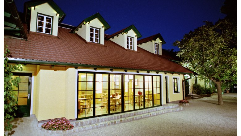 Ein Gebäude mit gelber Fassade und roten Dachziegeln bei Nacht, beleuchtet von innen.