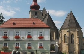 Historic building with red roof and church in the background on the Maria-Anzbach market square.