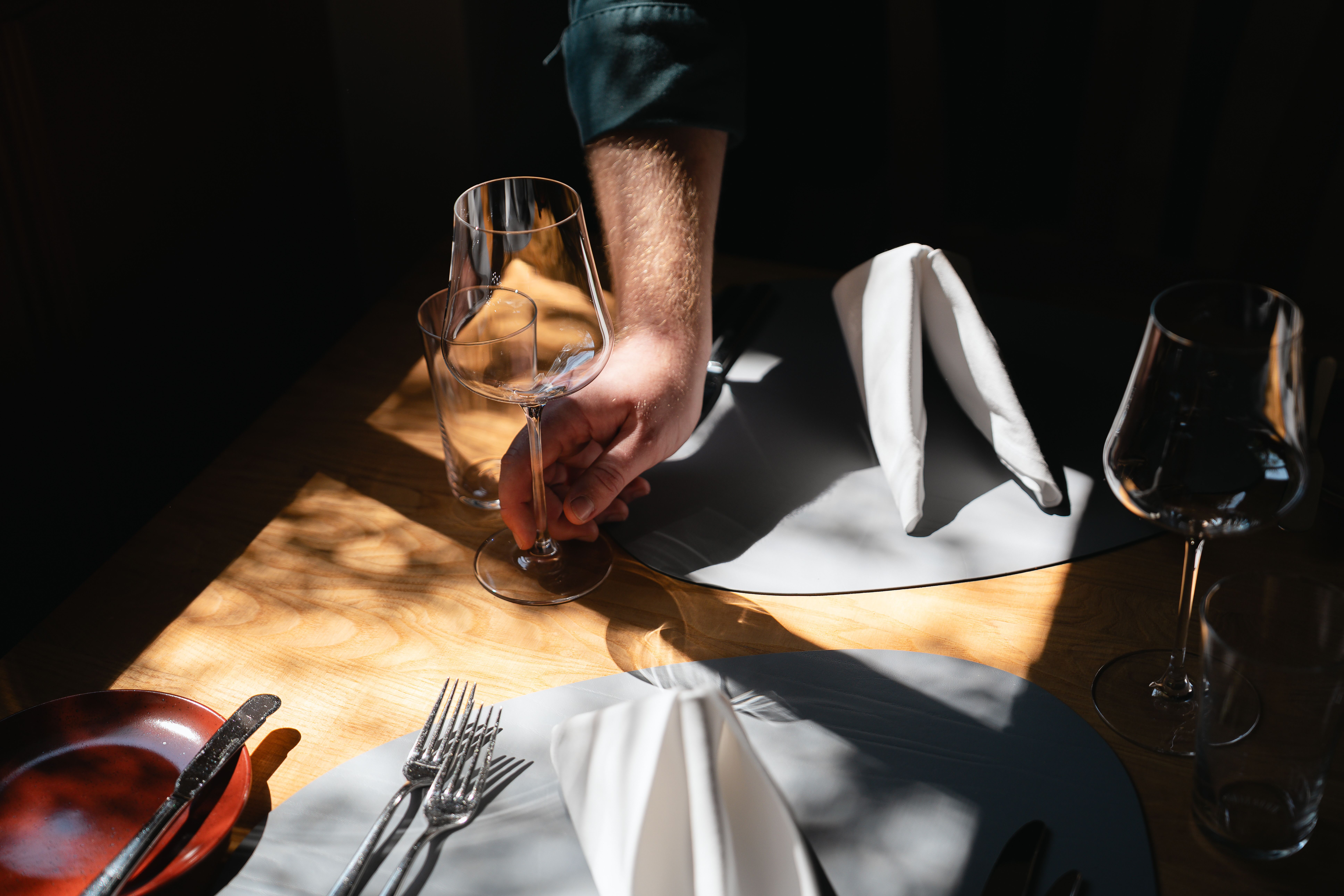 Nahaufnahme eines liebevoll gedeckten Holztisches im Restaurant Thomas im Johanneshof, leicht von Sonnenlicht durchflutet.