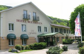 Außenansicht des Hotel Beethoven mit Café Fidelio, umgeben von Bäumen und Flaggen.
