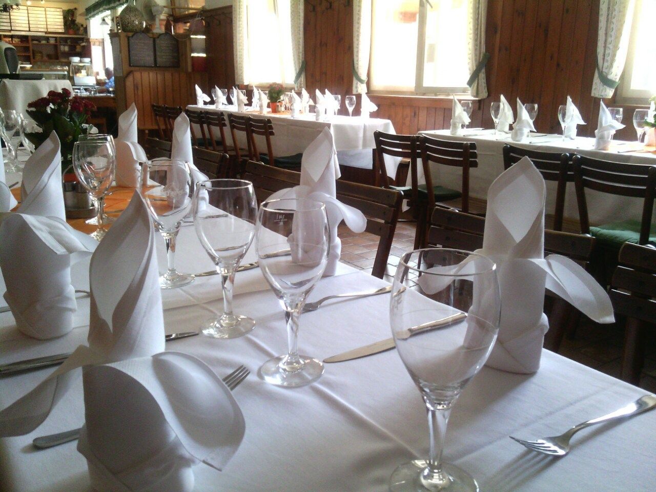 Festlich gedeckter Tisch mit weißen Tischdecken, Weingläsern und gefalteten Servietten in einem Restaurant.