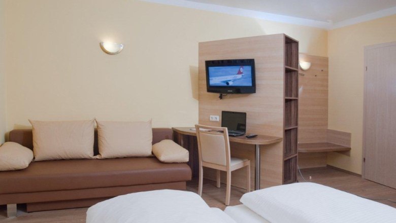 Hotelzimmer mit Sofa, Schreibtisch, Fernseher und Bett.