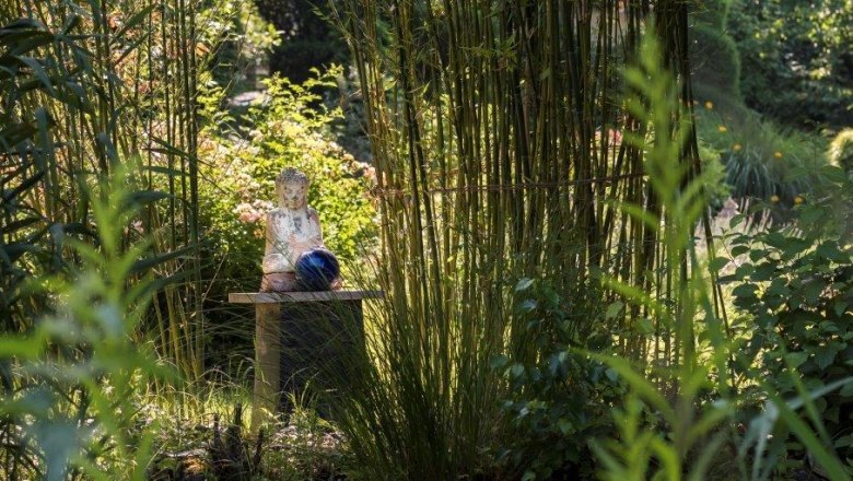 Ein asiatisch inspirierter Garten mit einer Buddha-Statue auf einem Tisch, umgeben von Bambus und üppigem Grün.