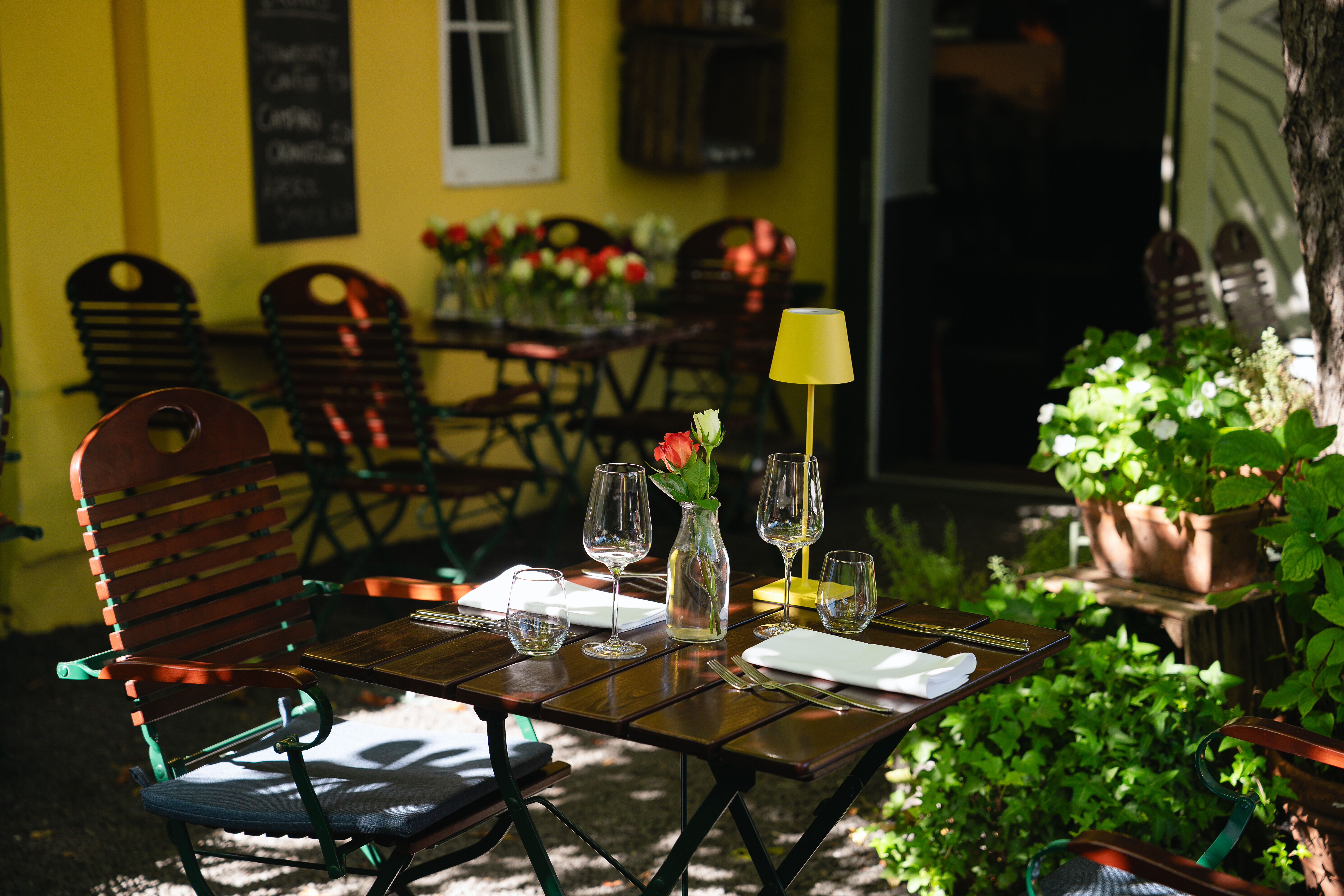 Blick auf den einladend gedeckten Gastgartentisch im Restaurant Allerley, umgeben von grünen Pflanzen und stilvollen Sitzgelegenheiten.