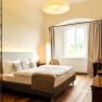 Elegant hotel room with double bed, wooden floor and large window.