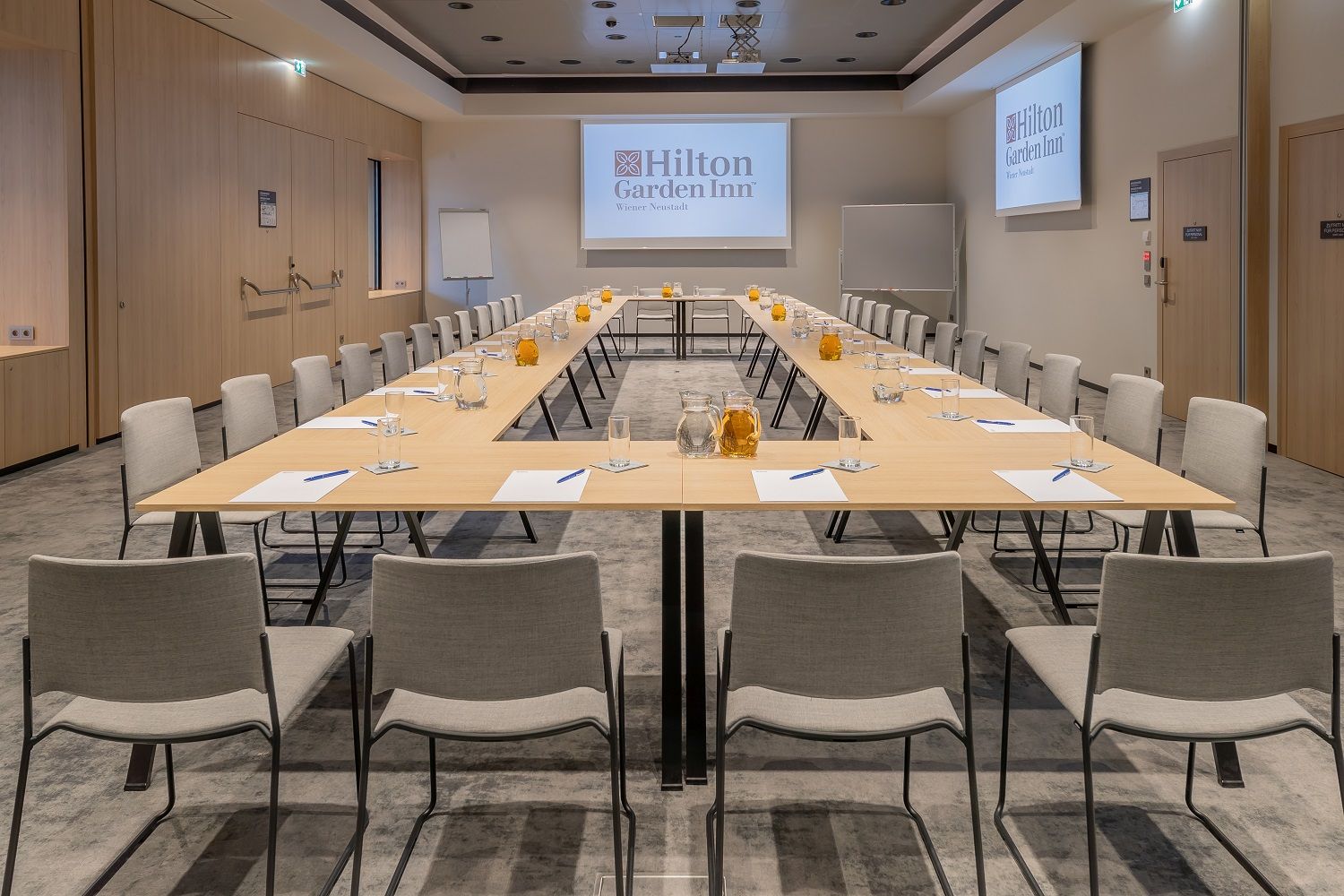 Ein moderner Meetingraum im Hilton Garden Inn mit U-förmiger Tischanordnung, Stühlen, Wasserkrügen und Schreibmaterialien.