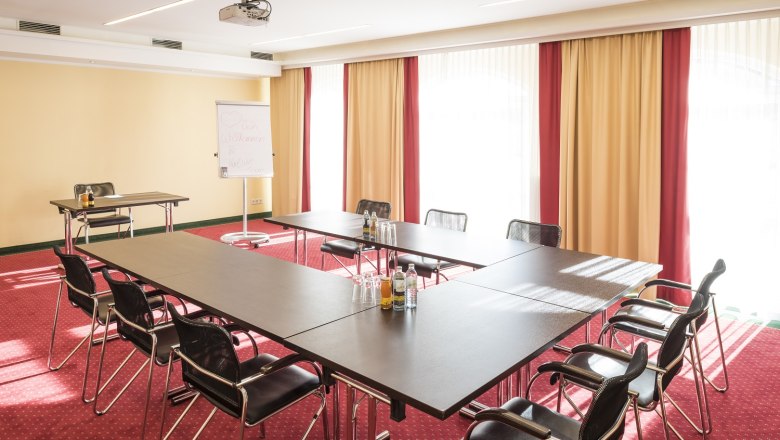 Konferenzraum mit U-förmigem Tisch, Stühlen, Flipchart und Projektor.