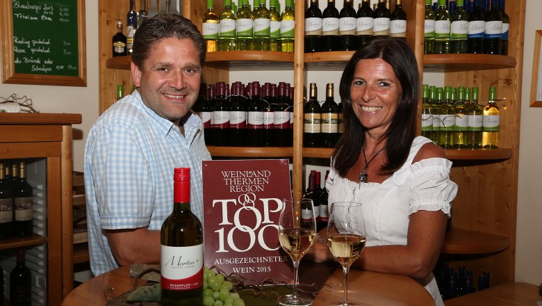 Zwei Personen in einem Weingeschäft mit Weinflaschen im Hintergrund.