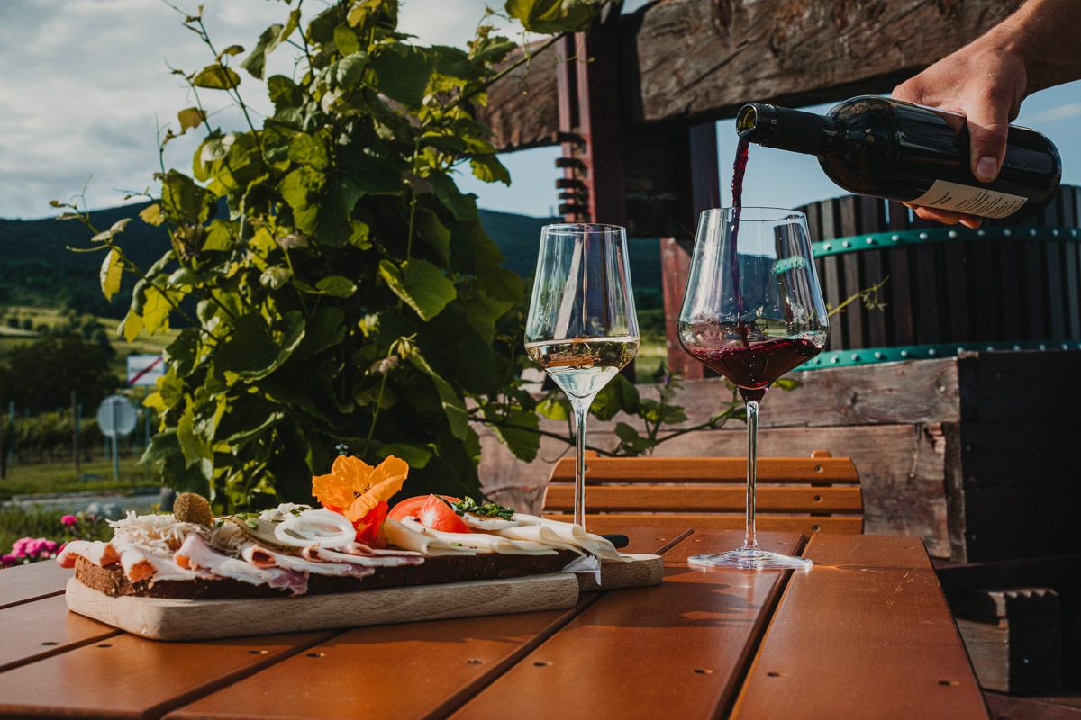 Rustikale Brettljause mit verschiedenen Fleischspezialitäten, liebevoll angerichtet und mit frischen Blumen dekoriert, serviert in einem sonnigen Heurigengarten an einem warmen Sommertag.