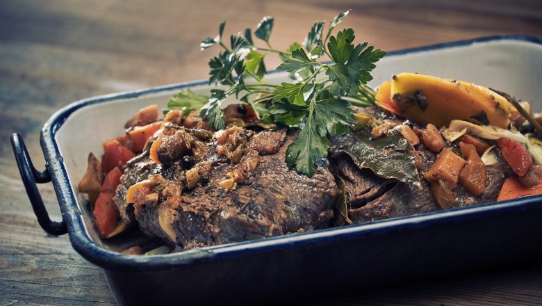 Ein Braten mit Gemüse und Kräutern in einer Auflaufform.